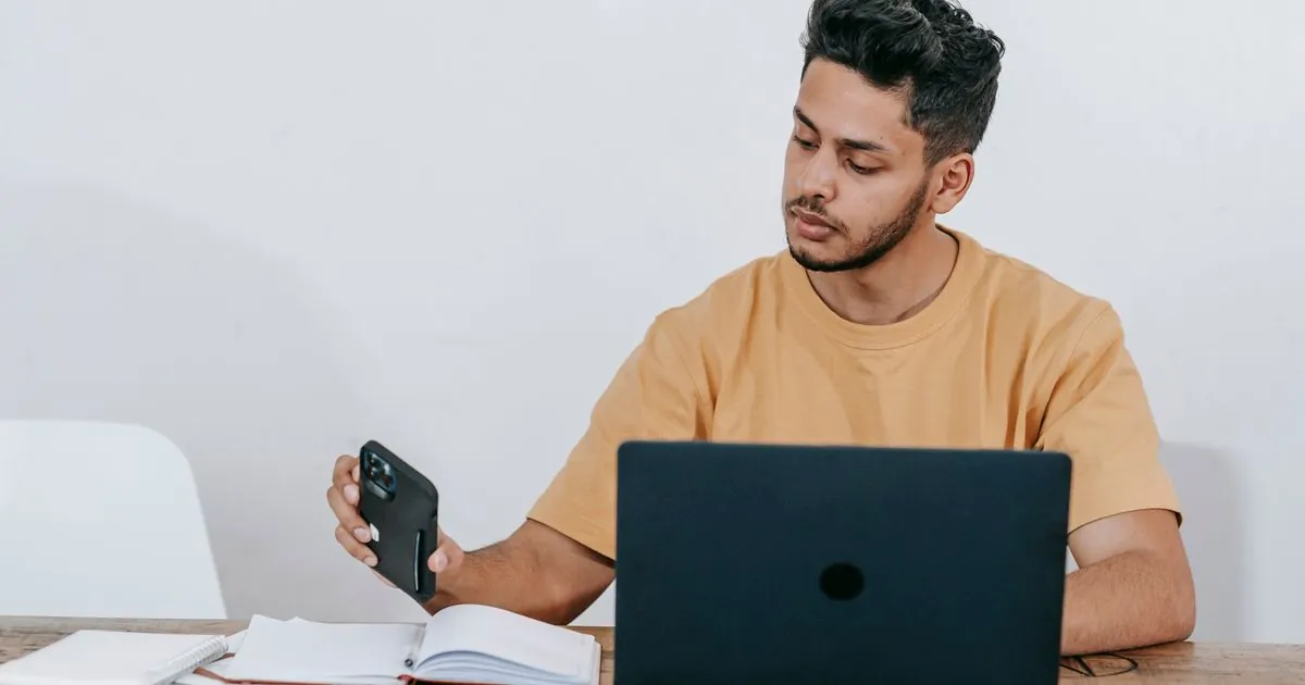 Borrower checking a loan application without bank verification documents on his phone beside a laptop