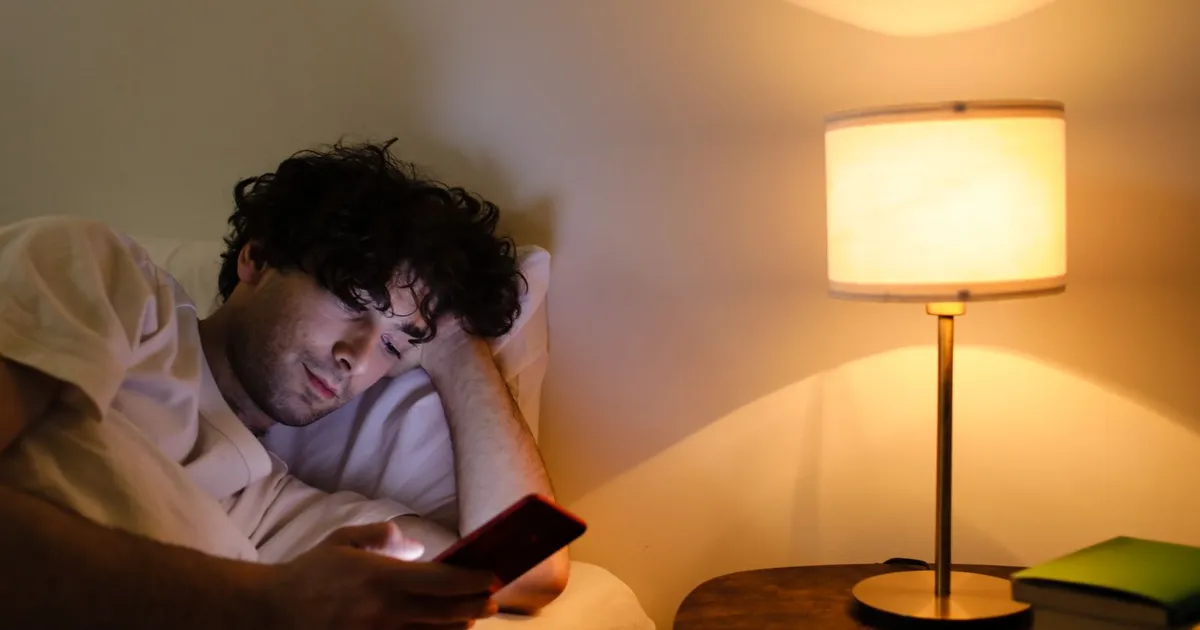 Late-night application for 24/7 loans on a phone in bed by lamplight
