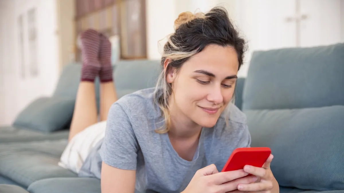 Femme souriante étendue sur son divan qui lit la décision de son prêt rapide sur son téléphone