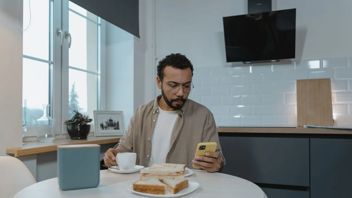 Homme à sa table de cuisine qui suit l'arrivée de son prêt rapide par Virement Interac sur son téléphone