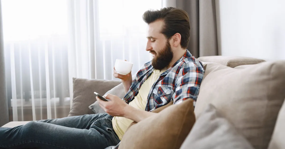 Man on his sofa with a coffee applying for weekend loans in Canada by phone on a Saturday morning
