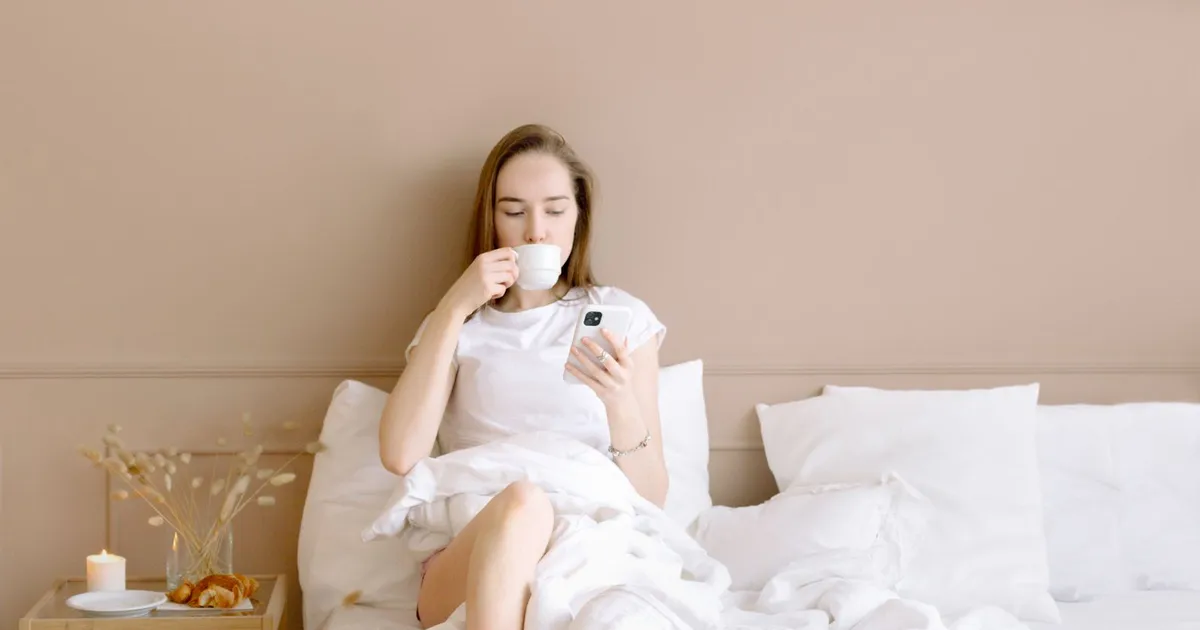 Woman in bed with coffee checking her phone on a Saturday morning for the decision on her weekend loans application