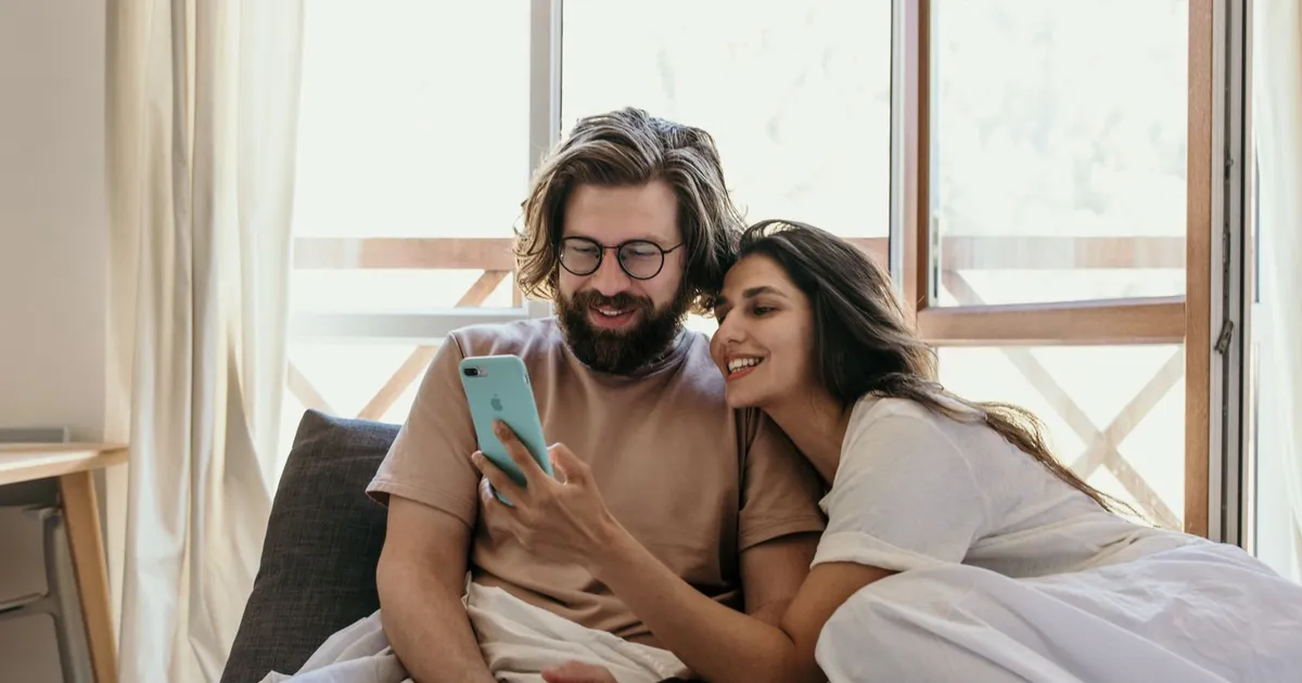 Couple in bed on a Sunday morning reading the decision on their weekend loans application on a phone